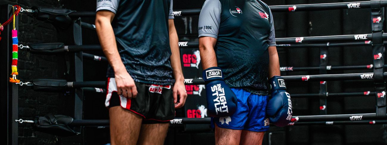 Two adult Muay Thai students standing ready in front of the GFC boxing ring