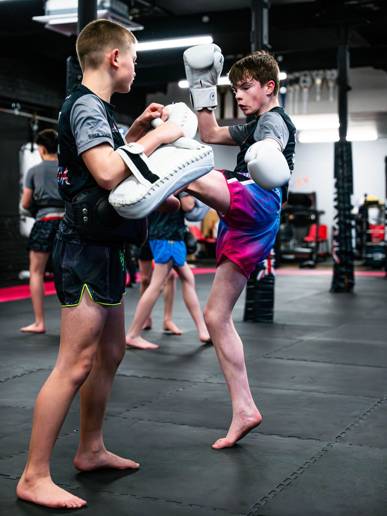A junior Muay Thai student drives a knee into body pads held by a training partner