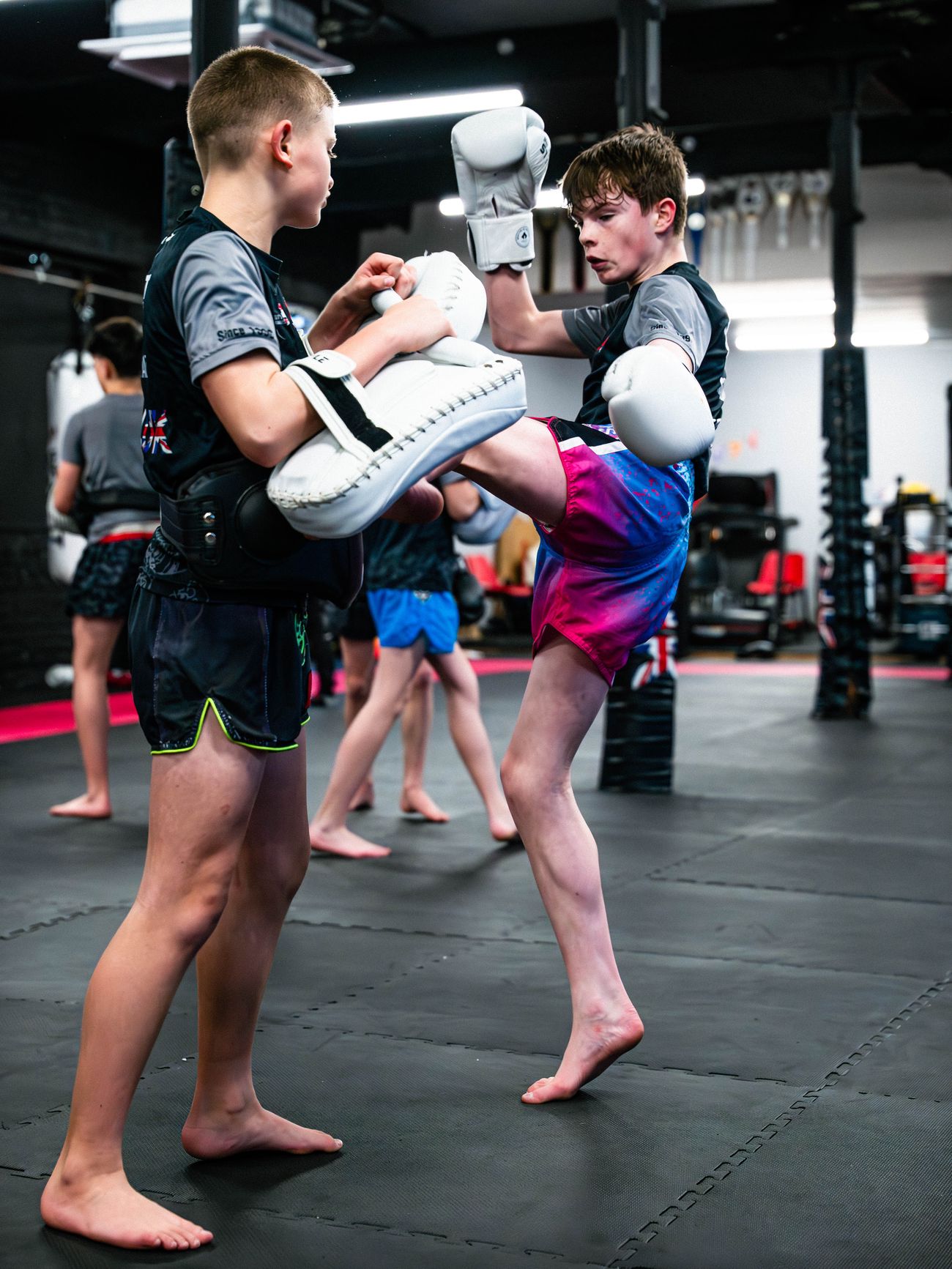 A junior Muay Thai student drives a knee into body pads held by a training partner