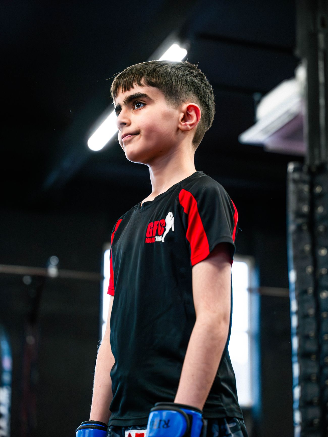 A young GFC Muay Thai student in blue gloves and a black and red training shirt