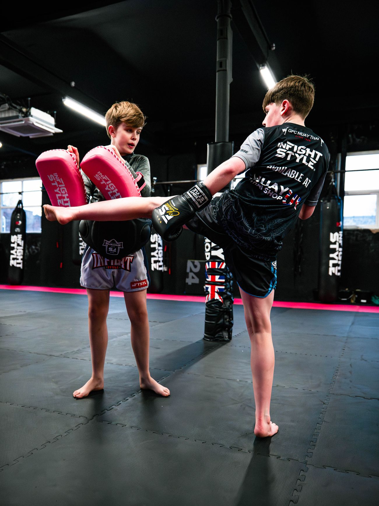 One junior Muay Thai student lands a roundhouse kick on pads held by another
