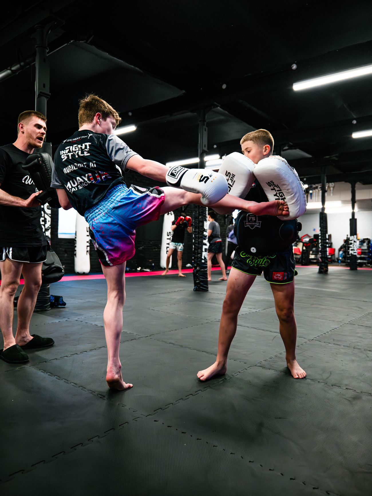 Luke Phillips watches two teen students practise a roundhouse kick with body pads