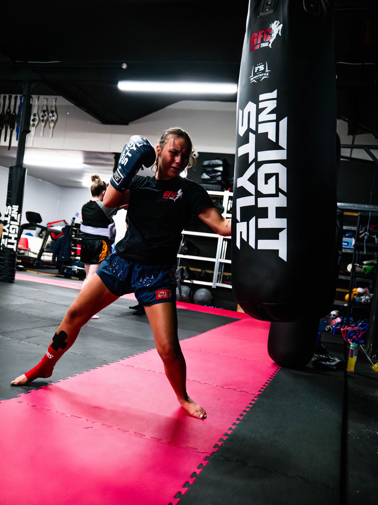 A woman in blue boxing gloves strikes an InFightStyle heavy bag at GFC Muay Thai